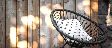 A wicker chair with a polka-dotted cushion against a wooden fence.