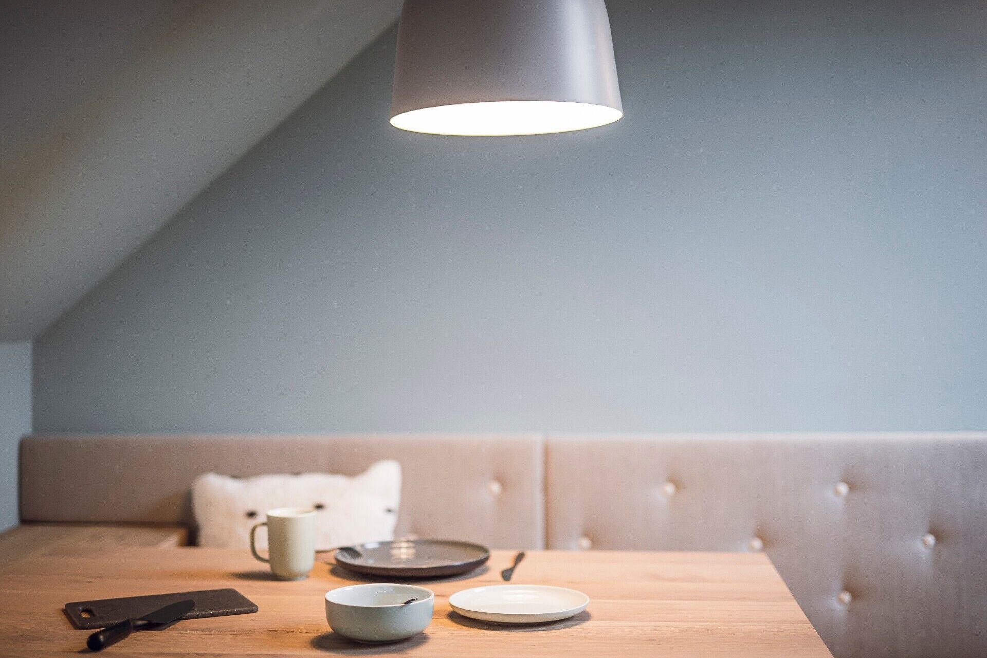A dining area with a table, a bench, a hanging light fixture, and a cup.