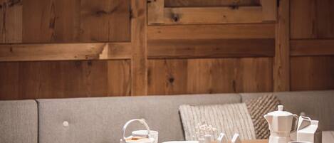 A wooden interior with a sofa, a dining table with white tableware, and a hanging light fixture.