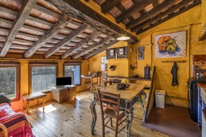 Uma cozinha rústica com vigas de madeira, uma mesa de jantar, cadeiras e um quadro na parede.
