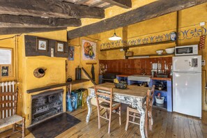 Uma cozinha rústica com vigas de madeira, lareira de pedra e um espaço de refeições com cadeiras de estilos variados.