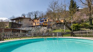 A swimming pool with a wooden fence, surrounded by stone buildings with balconies, and trees with pink blossoms.