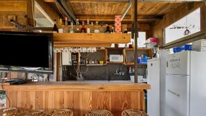 A rustic kitchen with wooden bar stools, a TV, and a refrigerator.