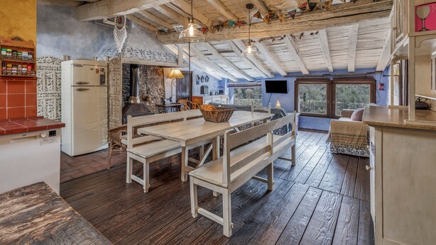 A rustic kitchen with wooden beams, a dining area with benches, a television, and a view through a window. - Vacation Home "Els Mossos, El Reixac Casa Rural" with Mountain View, Shared Pool & Wi-Fi (Sant Joan de les Abadesses)