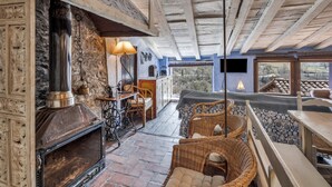 A rustic interior with a stone fireplace, wicker furniture, and a view through the windows. - Vacation Home "Els Mossos, El Reixac Casa Rural" with Mountain View, Shared Pool & Wi-Fi (Sant Joan de les Abadesses)