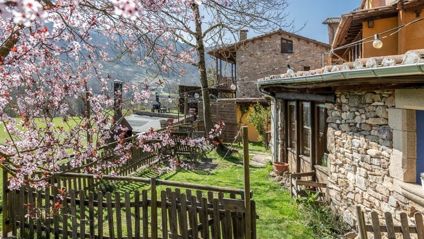 A rustic stone building with a wooden fence, a stone wall, and a view of a mountain in the background.