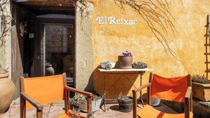 An outdoor seating area with two orange chairs, a small table with a potted plant, and a wall with the name 'ElReixac'.