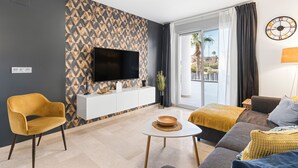 A modern living room with a flat-screen TV, a sofa, a yellow armchair, a small table, and a patterned wall. - Sungolfbeach El Girasol (orihuela)