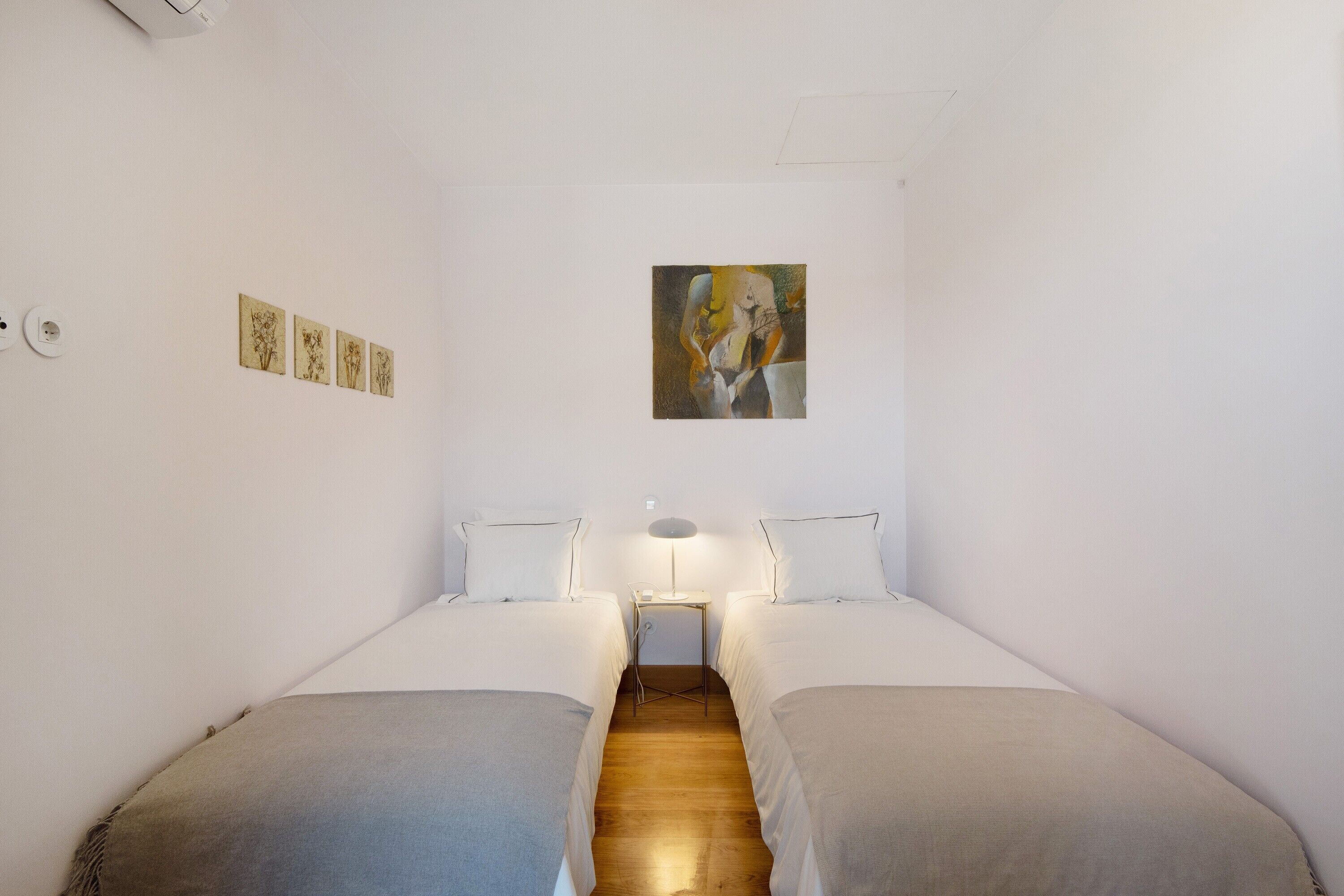 Ein Zimmer mit zwei Betten, einem kleinen Tisch mit einer Lampe und einem Bild an der Wand.