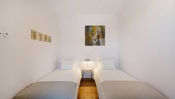 Ein Zimmer mit zwei Betten, einem kleinen Tisch mit einer Lampe und einem Bild an der Wand.