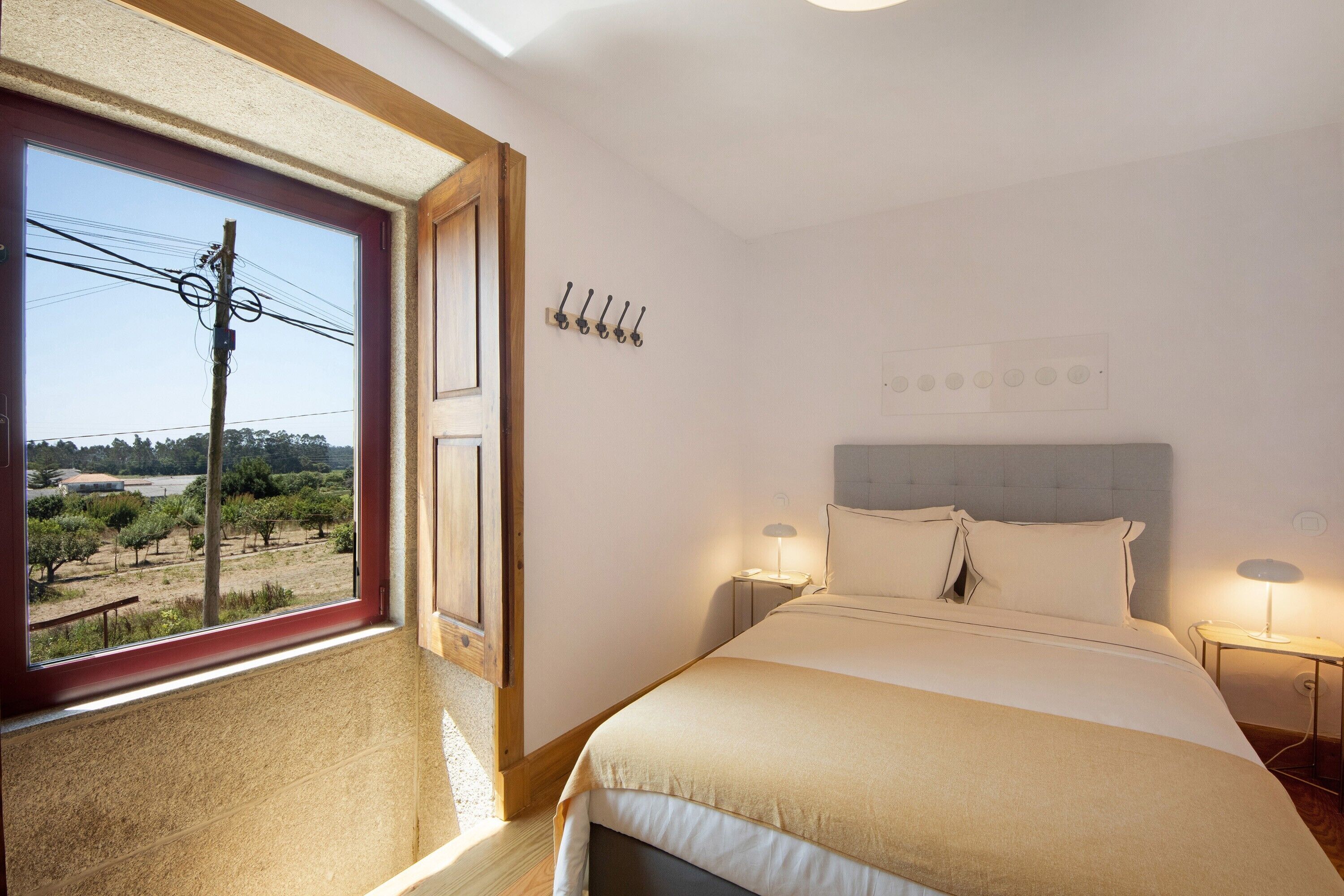Een slaapkamer met een groot raam, een bed, nachtkastjes en een wandlamp.