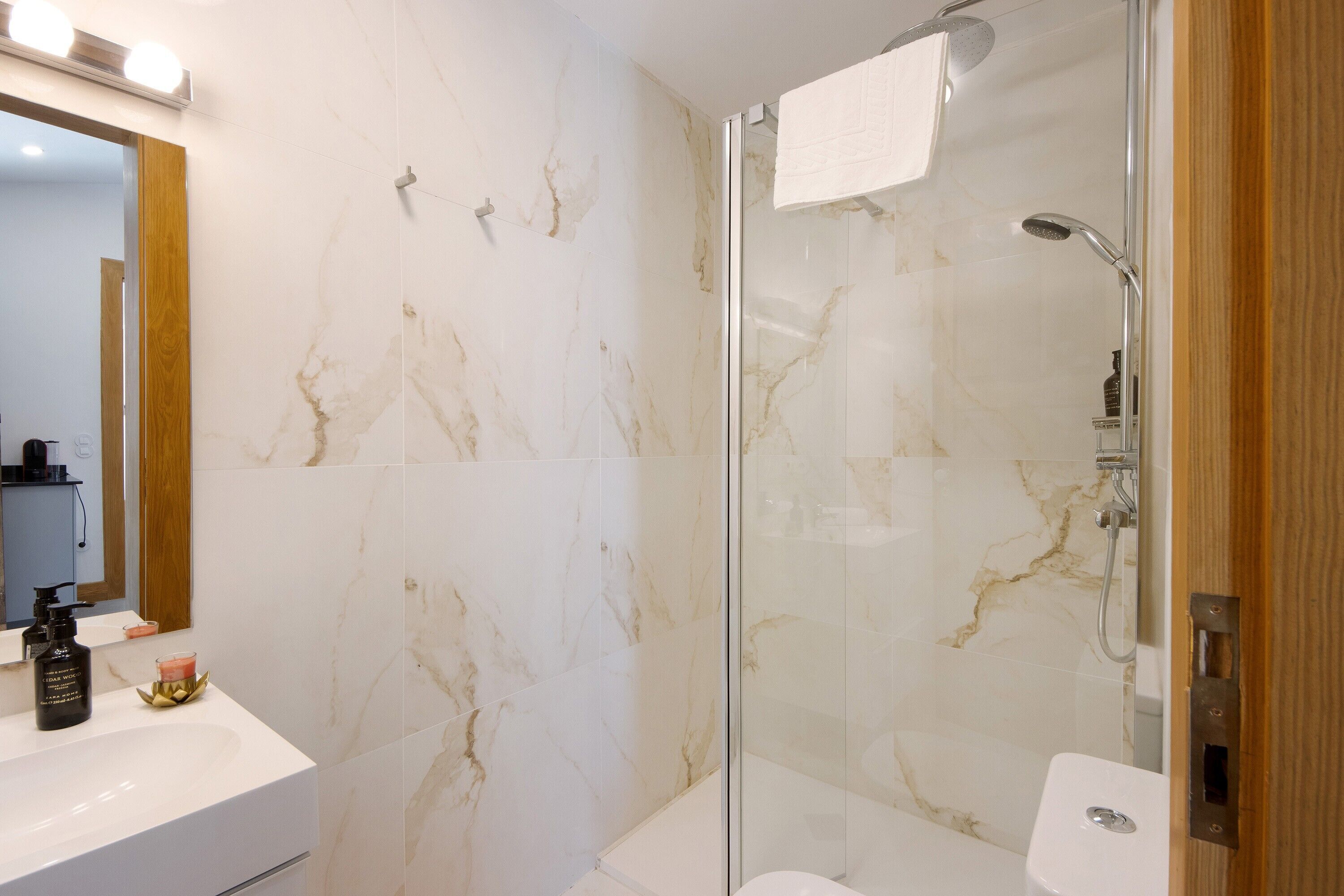 A bathroom with a glass-enclosed shower, a white sink, and a mirror with lights.