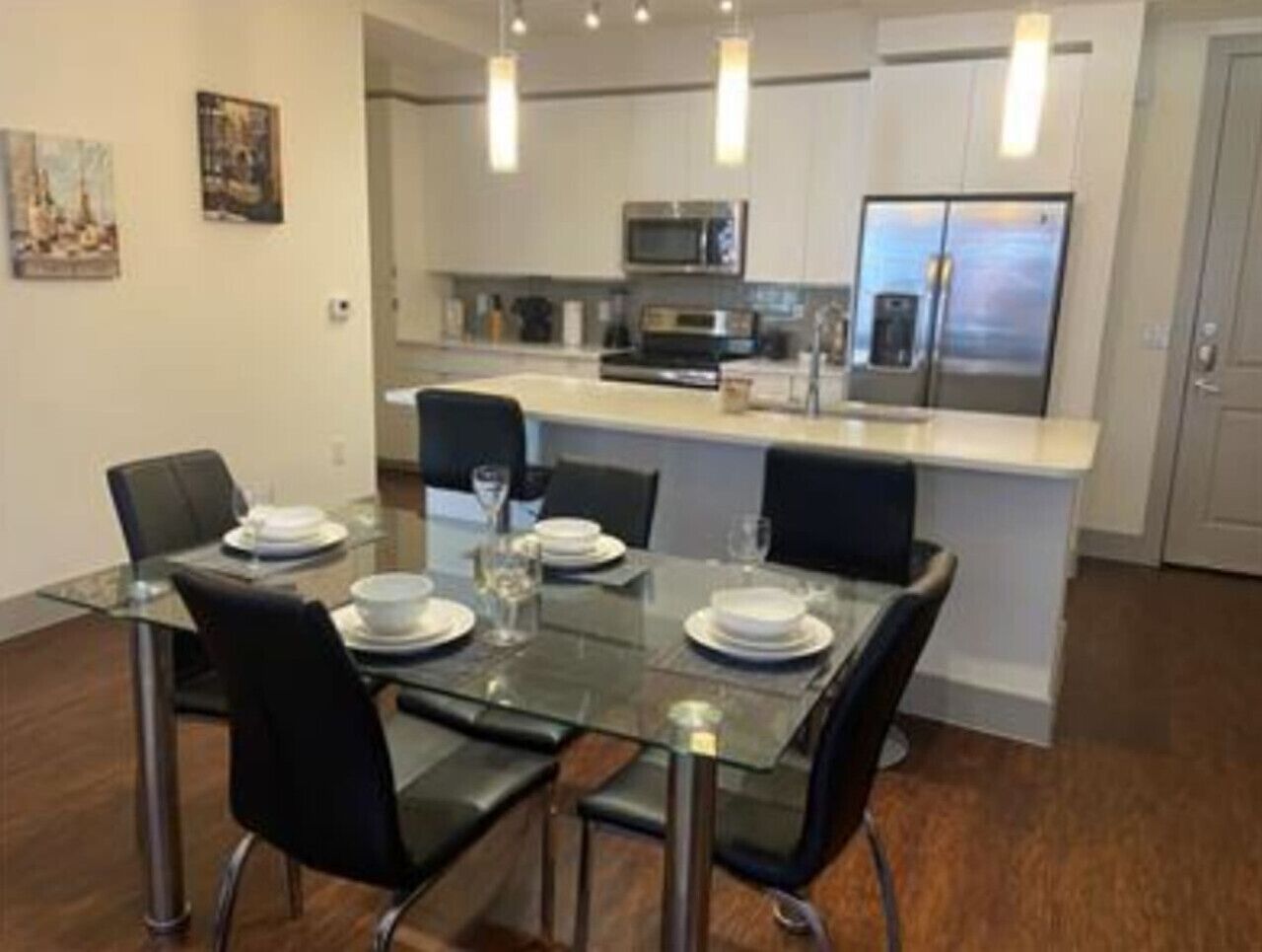 Une cuisine moderne avec des meubles blancs, des appareils en acier inoxydable et une table à manger en verre, assortie de chaises noires.