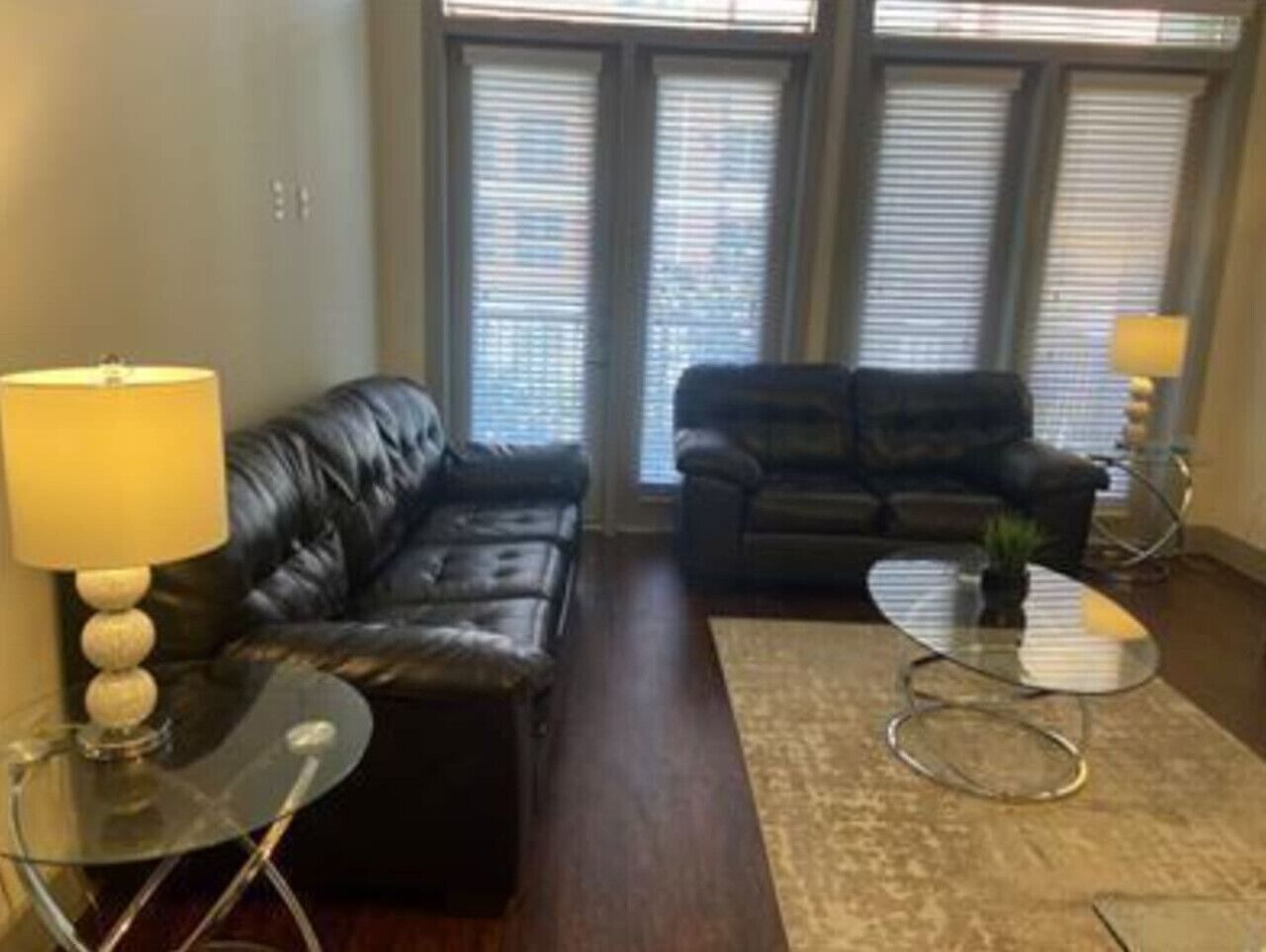 A living room with two black leather sofas, a glass coffee table, and a lamp on a side table.