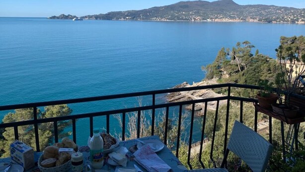 Ein Balkon mit Blick auf ein ruhiges Meer, ein Berg in der Ferne und ein Tisch mit Speisen.