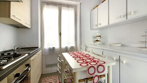Eine Küche mit einem Gaskochfeld, weißen Schränken, einem Fenster mit Vorhängen und einem kleinen Tisch mit einer rot-weißen Tischläufer.