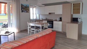 Una cocina moderna con armarios blancos, una mesa de comedor con sillas, un sofá rojo y vistas al exterior.