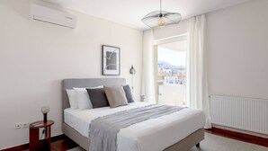 Une chambre à coucher avec un lit, une table de chevet, une lampe, un tableau au mur et une fenêtre donnant sur un beau paysage.