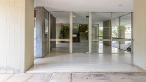 Une entrée moderne avec des portes en verre, un pilier en béton et une vue sur un escalier menant à un espace de stationnement.