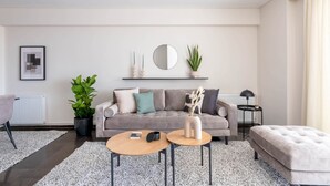 Un salon moderne avec un canapé gris, deux petites tables rondes, une plante en pot et un miroir au mur.