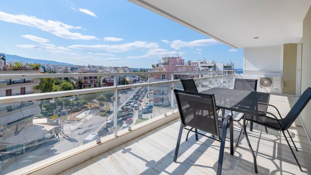 Un balcon avec une table et des chaises, donnant sur un paysage urbain et une étendue d’eau.