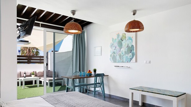A bedroom with a bed, a desk, a chair, a bench, and a sliding glass door leading to an outdoor seating area. - Studio "Dannamar" near the beach with private terrace and Wi-Fi (Puerto del Carmen)