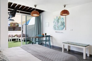 A bedroom with a bed, a desk, a chair, a bench, and a sliding glass door leading to an outdoor seating area.