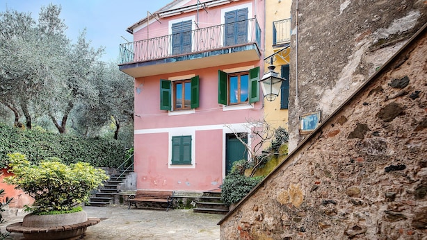 A pink building with green shutters, a stone staircase, and a potted plant.