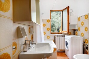 Une petite salle de bain comprenant un lavabo, un lave-linge et une fenêtre donnant sur un espace verdoyant.