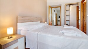 A hotel room with a wooden headboard, a bedside table with a lamp, a large bed with white linens, and a wardrobe with a mirror.