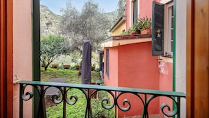 A balcony with a view of a garden and a hillside.