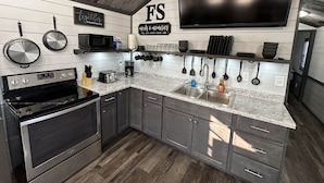 A modern kitchen with stainless steel appliances, a granite countertop, and a large flat-screen TV mounted above the sink. - FS Rental #3 Annapolis, MO Black River (Annapolis)