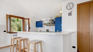 Eine Küche mit weißer Arbeitsplatte, Holzstühlen, einer Uhr und einer Holztür.