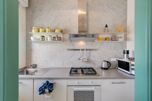 Een keuken met een gasfornuis, oven, magnetron en diverse keukengerei op planken.
