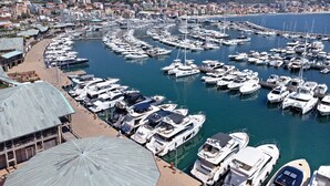 Un port de plaisance où sont amarrés de nombreux bateaux, une promenade en bord de mer et des bâtiments en arrière-plan.