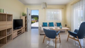 Una sala de estar moderna con un televisor de pantalla plana, un sofá con cojines color turquesa, una mesa de comedor y vistas al exterior.