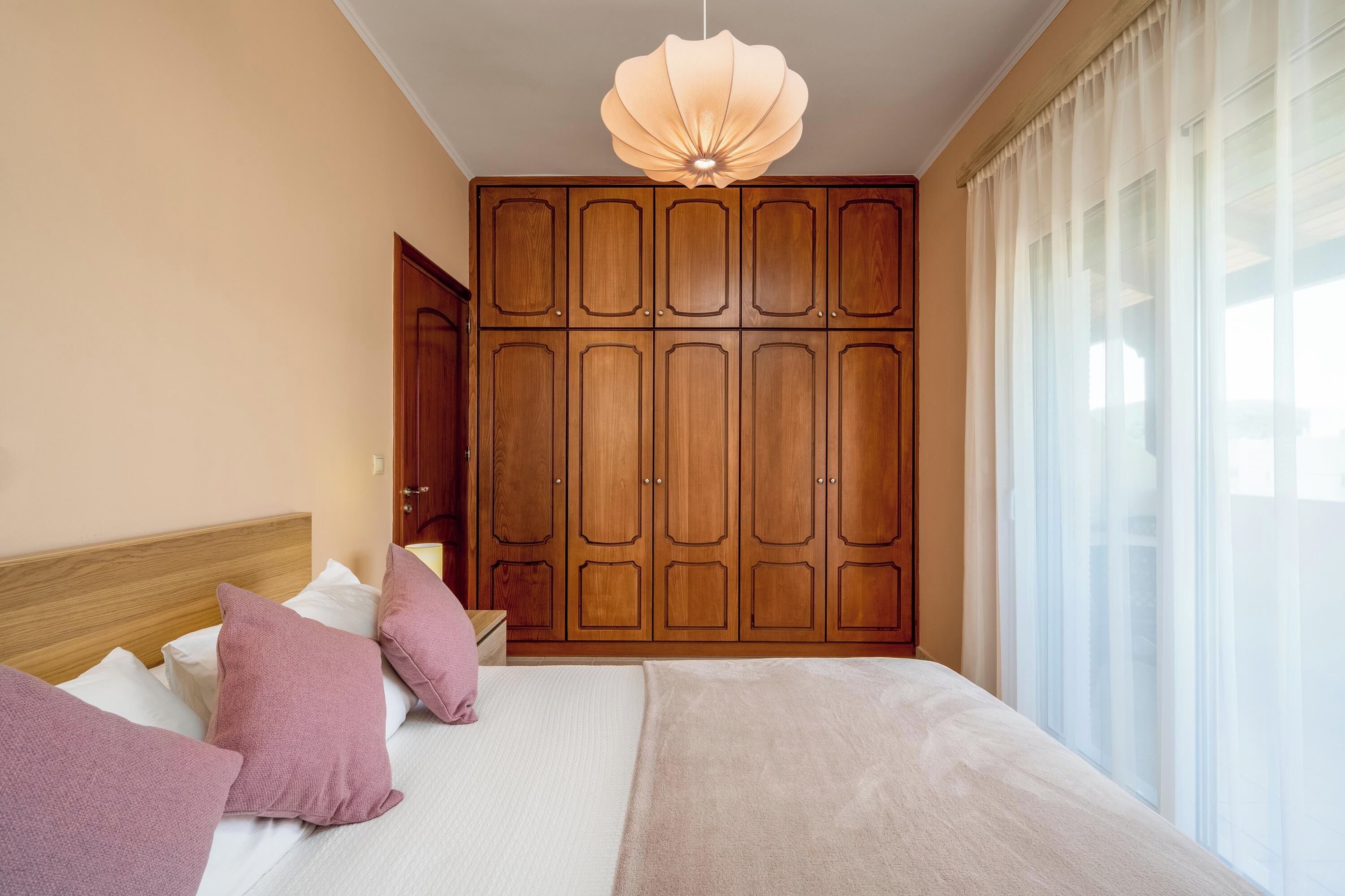 Une chambre avec un grand lit, une armoire en bois et un luminaire suspendu.