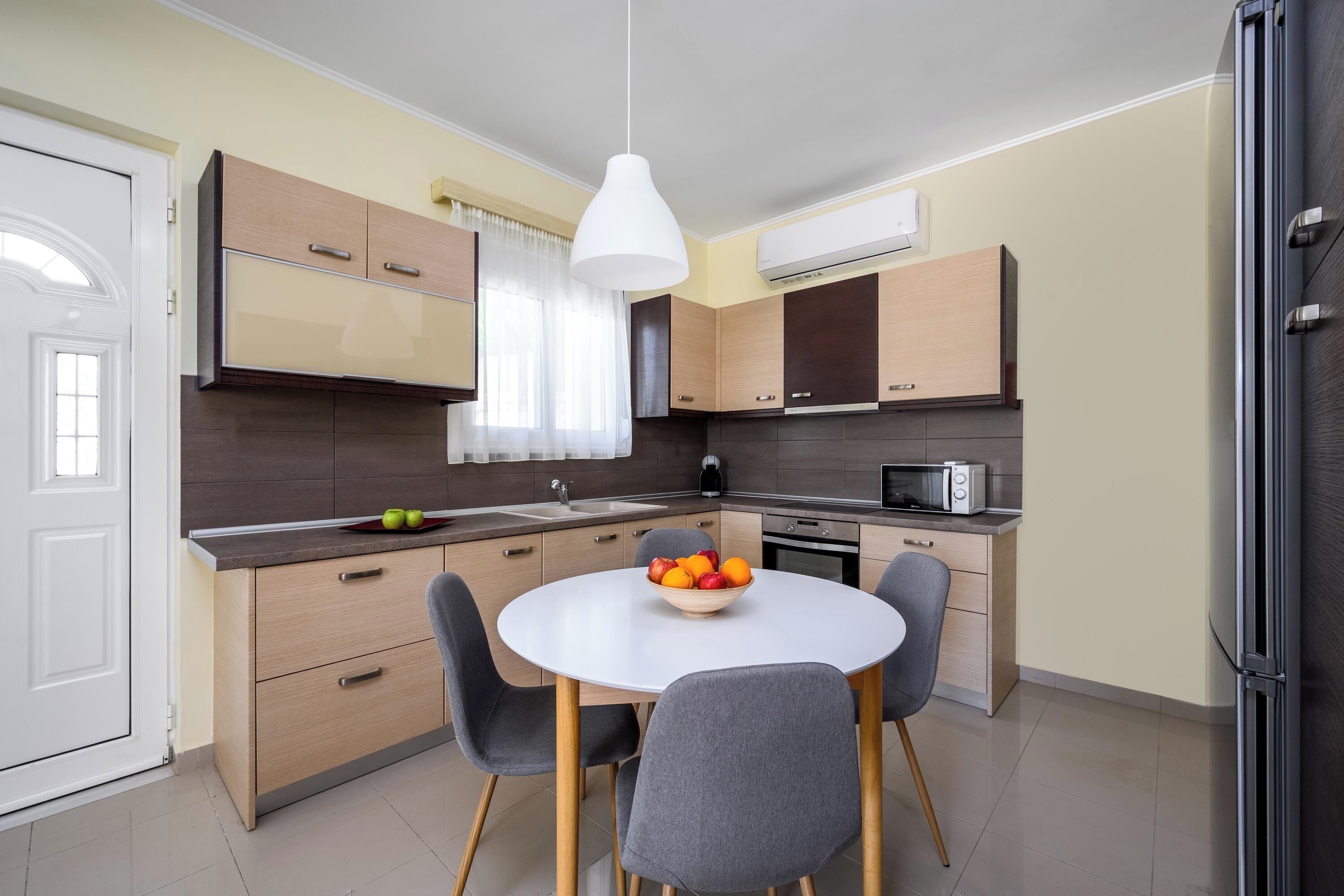 Une cuisine moderne avec un coin repas, comprenant une table blanche, des chaises grises et un saladier rempli de fruits.