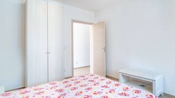 A bedroom with a bed, a wardrobe, a bench, and an open door leading to a balcony.