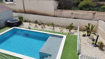 A rectangular swimming pool with a tiled edge, surrounded by artificial grass and a gravel area with small plants.