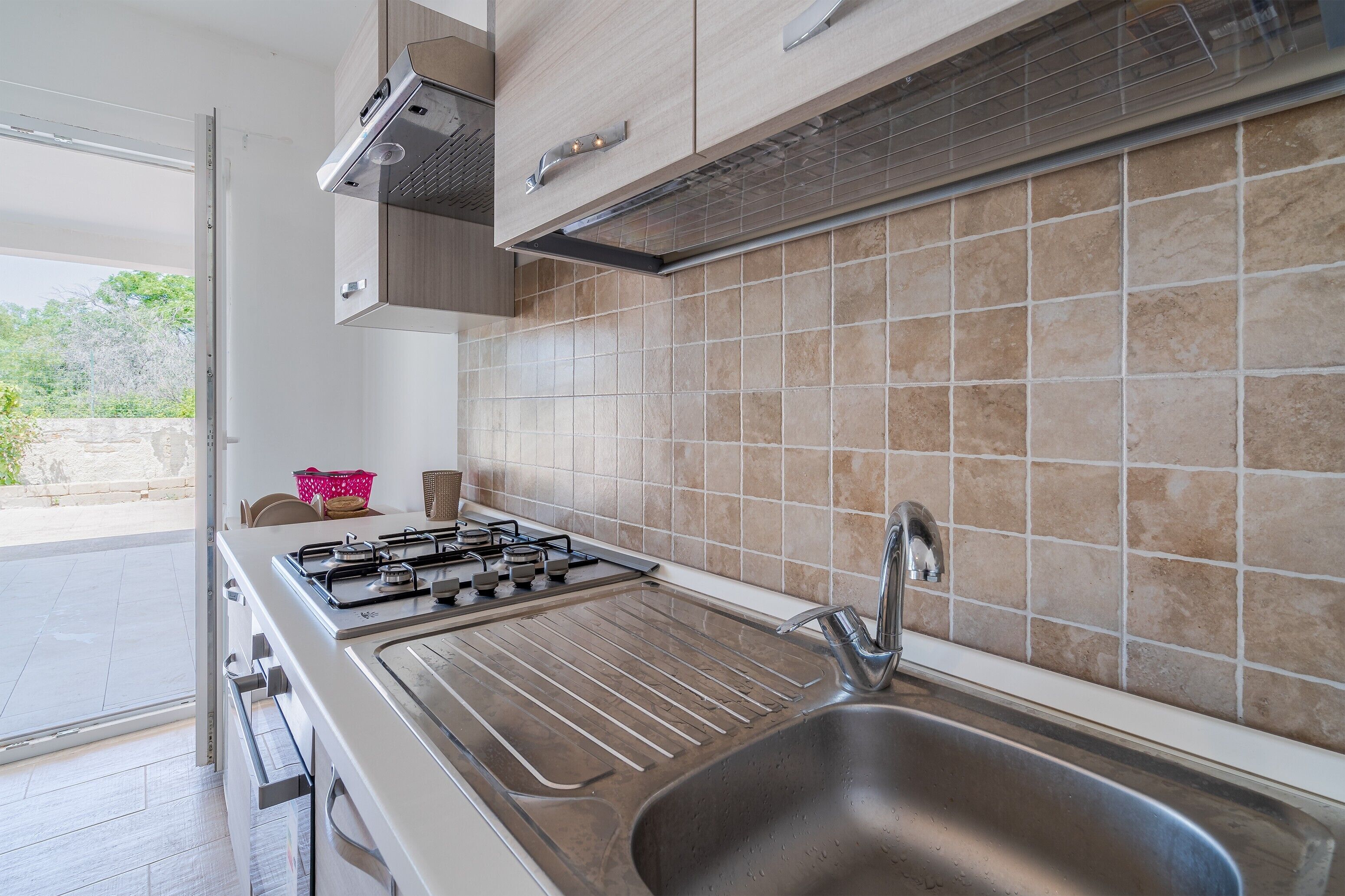 A modern kitchen with a gas stove, stainless steel sink, and light-colored tiles.