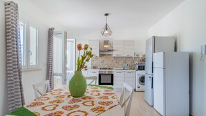 Ett modernt kök med ett matbord, stolar, en vas med blommor, en tvättmaskin och ett kylskåp.