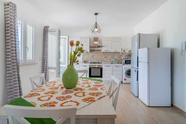 Une cuisine moderne avec une table à manger, des chaises, un vase de fleurs, un lave-linge et un réfrigérateur.