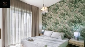 Een slaapkamer met een bed, twee nachtkastjes, een raam met gordijnen en een muur met een bladerpatroon.