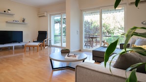 A modern living room with a flat-screen TV, a sofa, a coffee table, and a dining area with a table and chairs. - Vouliagmeni Honeymoon Suite (Βουλιαγμένη)