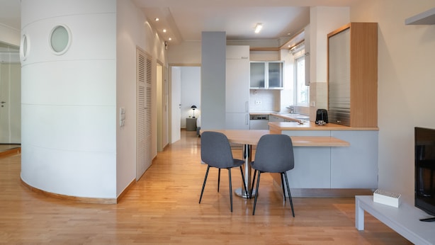A modern kitchen with a central island, a dining area with two chairs, and a TV on a stand. - Vouliagmeni Honeymoon Suite (Βουλιαγμένη)