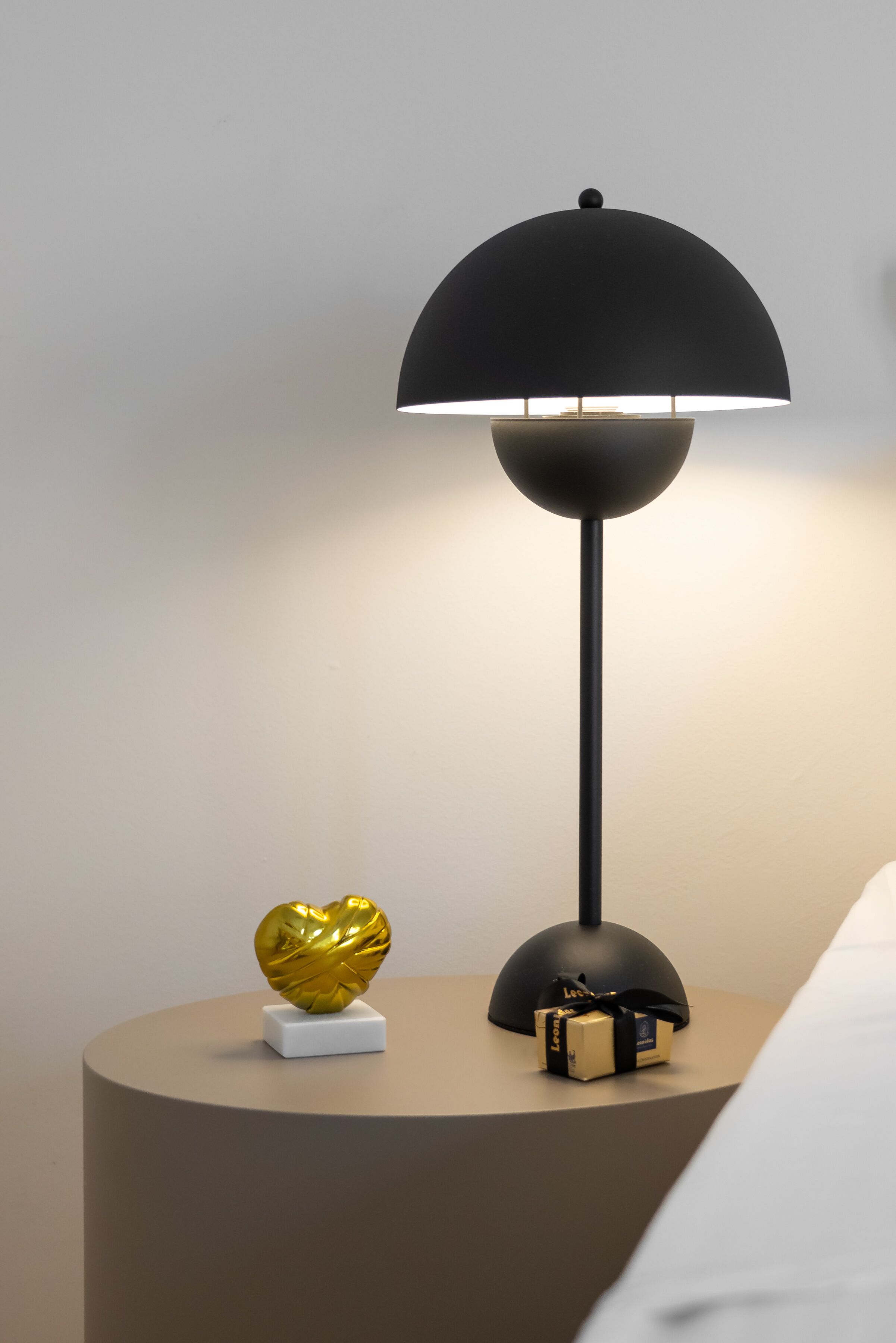 Ein moderner Nachttisch mit einer schwarzen Lampe, einem goldfarbenen herzförmigen Gegenstand und einer kleinen Geschenkbox.