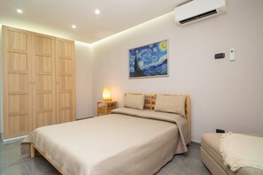 Une chambre à coucher comprenant un lit, des tables de chevet, une commode, un climatiseur, un tableau et une armoire.