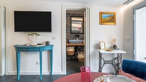 Un salón moderno con una televisión de pantalla plana, una mesa azul, una mesa roja, una máquina de coser y un sofá azul.