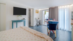 Un dormitorio con cama, televisor, escritorio, silla y zona de comedor con mesa y cortinas.